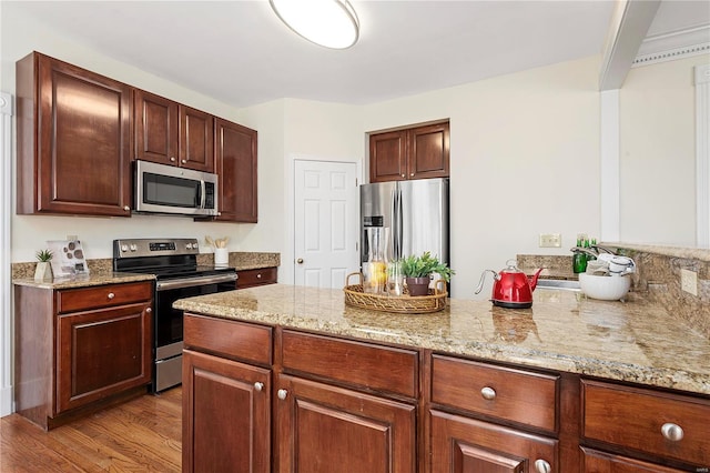 kitchen featuring light stone countertops, a peninsula, light wood-style floors, stainless steel appliances, and a sink