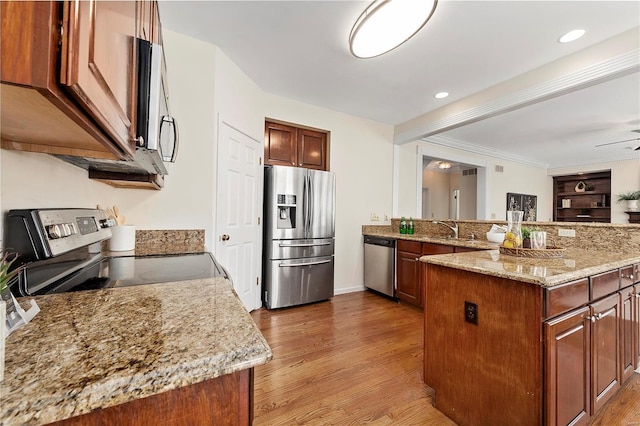 kitchen with light stone counters, a peninsula, light wood-style flooring, a sink, and appliances with stainless steel finishes