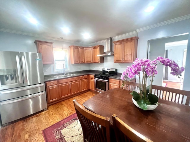 kitchen featuring dark countertops, light wood-style floors, stainless steel appliances, wall chimney exhaust hood, and a sink