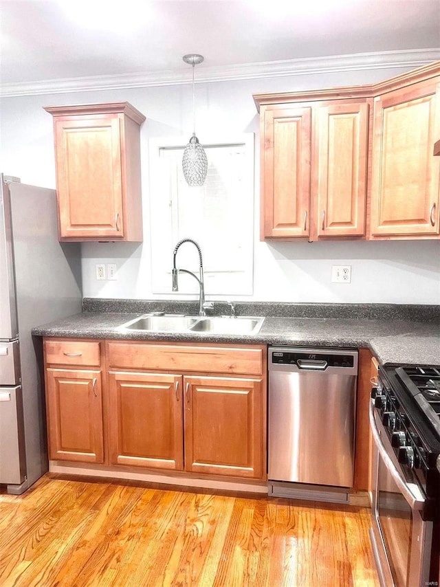 kitchen featuring dark countertops, light wood finished floors, ornamental molding, stainless steel appliances, and a sink