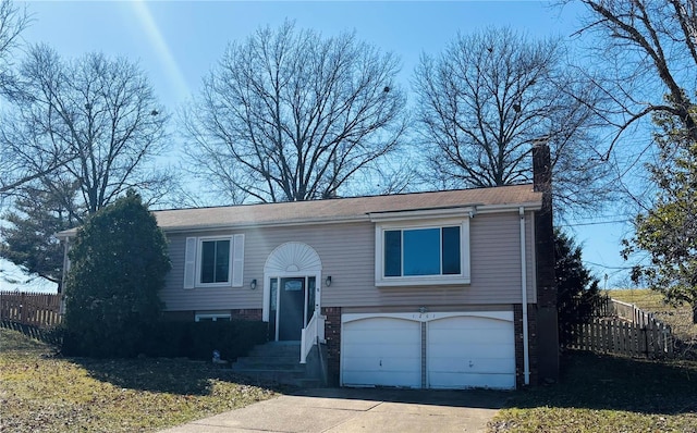 bi-level home featuring driveway, a chimney, an attached garage, and fence