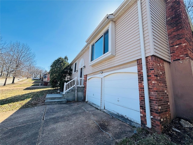 view of home's exterior with a garage, brick siding, and driveway