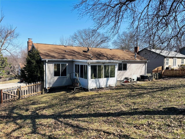 back of house featuring fence, a lawn, a sunroom, and a chimney