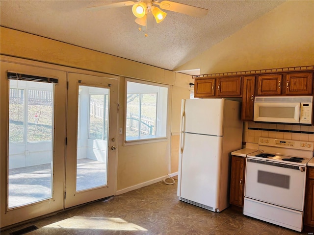 kitchen with ceiling fan, vaulted ceiling, brown cabinetry, white appliances, and a textured ceiling