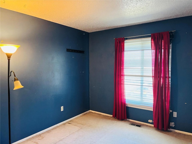 spare room featuring visible vents, baseboards, a textured ceiling, and carpet flooring