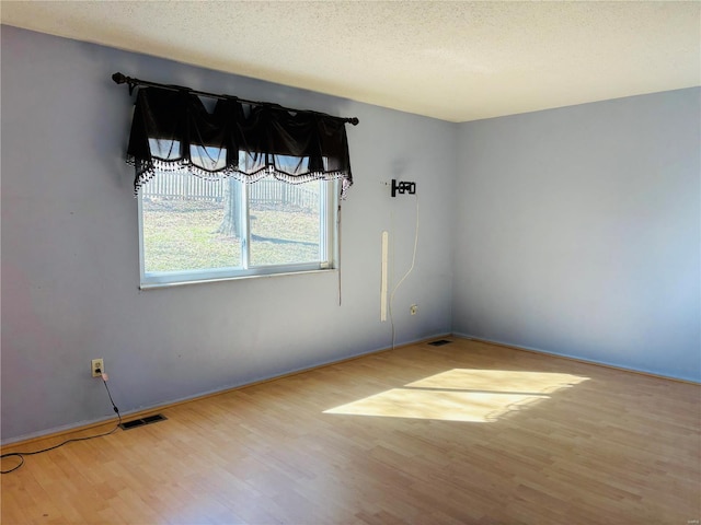 empty room featuring visible vents, a textured ceiling, and wood finished floors