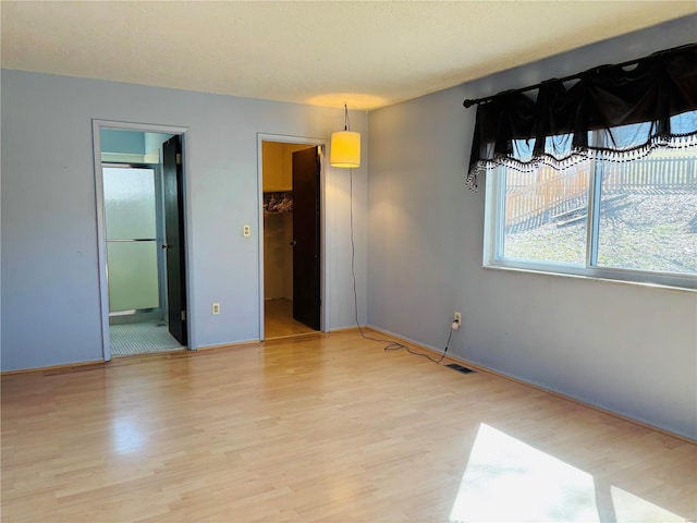 unfurnished bedroom with visible vents, ensuite bath, light wood-style flooring, and a spacious closet