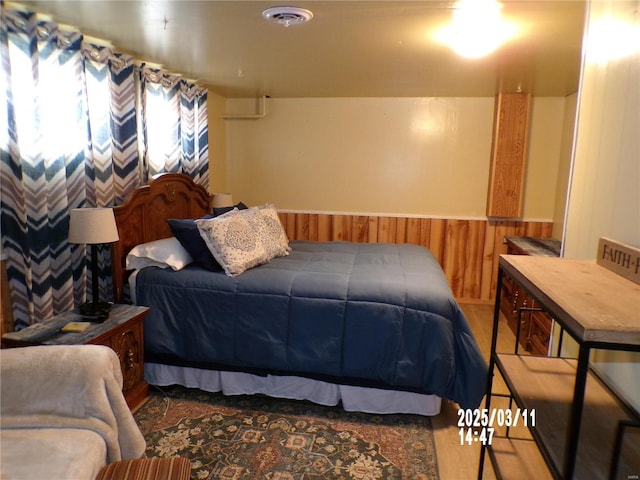 bedroom with visible vents, wood walls, and wainscoting