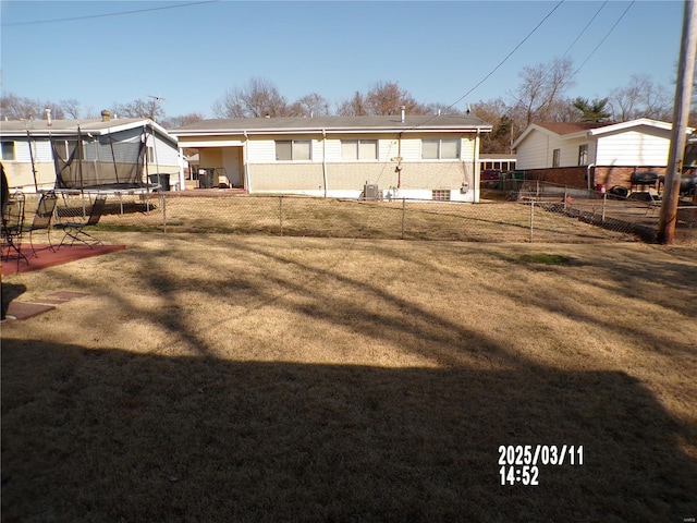 back of property featuring a yard, a trampoline, and a fenced backyard