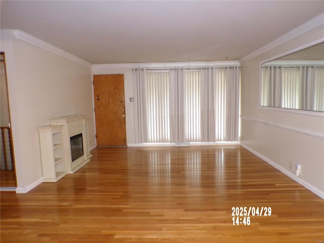 unfurnished living room featuring crown molding, baseboards, a glass covered fireplace, and wood finished floors