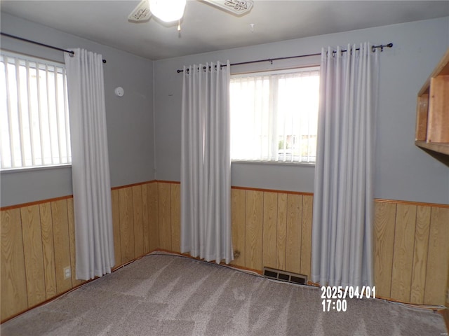spare room with carpet floors, a ceiling fan, wainscoting, and wood walls