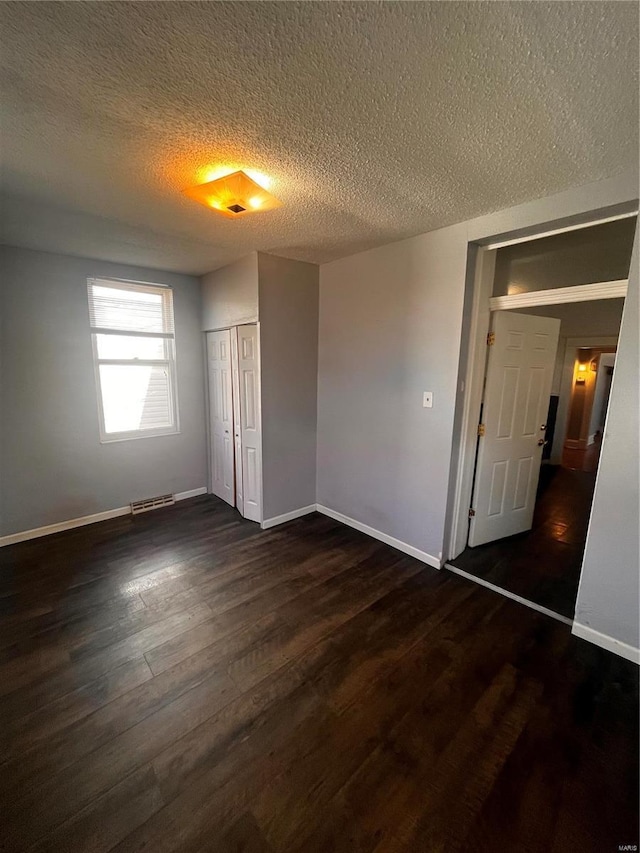 unfurnished bedroom with visible vents, baseboards, a closet, dark wood-style floors, and a textured ceiling