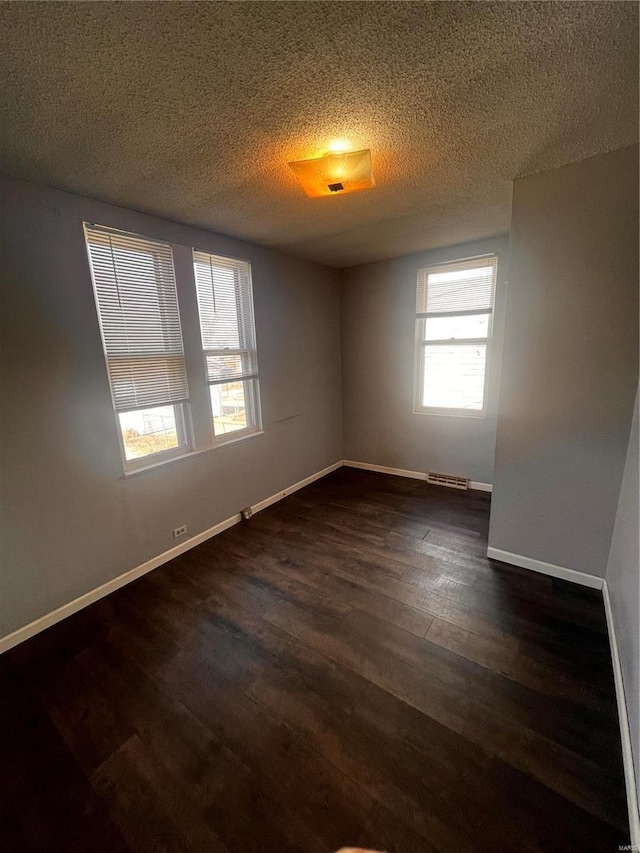 empty room with visible vents, baseboards, a textured ceiling, and dark wood-style floors