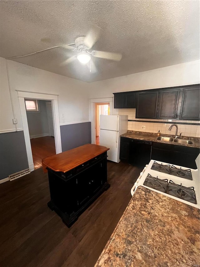 kitchen with dark countertops, backsplash, dark wood-type flooring, white appliances, and a sink