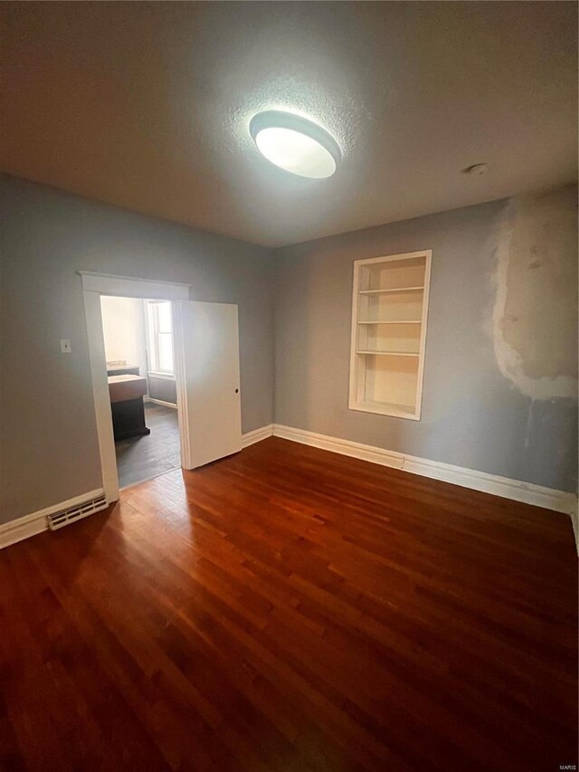 empty room with visible vents, built in shelves, a textured ceiling, wood finished floors, and baseboards