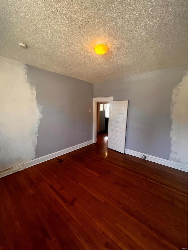 empty room with baseboards, a textured ceiling, and wood finished floors