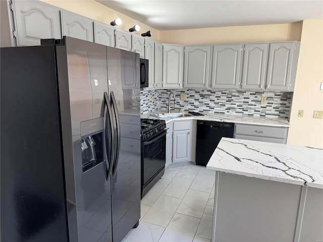 kitchen with decorative backsplash, black appliances, light stone counters, and a sink