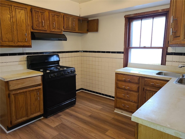 kitchen with brown cabinetry, dark wood finished floors, light countertops, black gas range, and under cabinet range hood