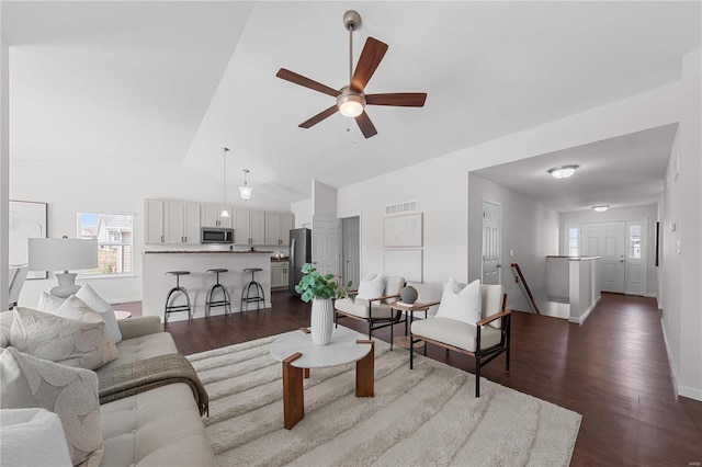 living area with dark wood-type flooring, a ceiling fan, visible vents, and vaulted ceiling