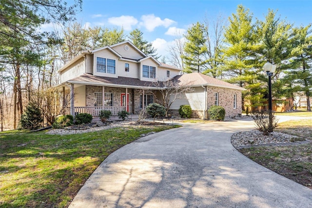 view of front facade with a front yard, brick siding, covered porch, and driveway