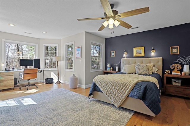 bedroom with multiple windows, an accent wall, baseboards, and wood finished floors