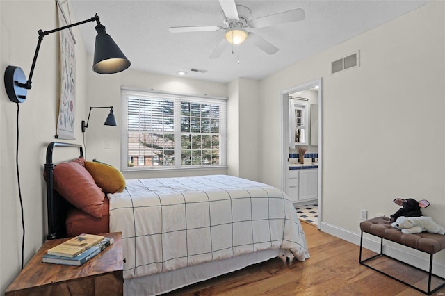 bedroom featuring visible vents, ceiling fan, baseboards, ensuite bathroom, and wood finished floors