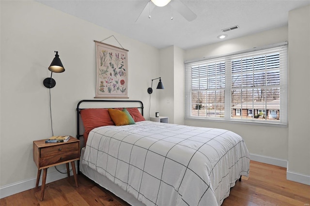 bedroom featuring visible vents, a ceiling fan, baseboards, and wood finished floors