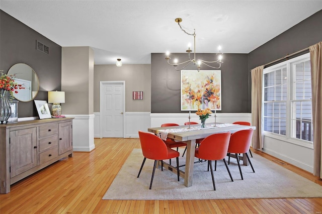 dining room featuring a notable chandelier, light wood-type flooring, visible vents, and wainscoting