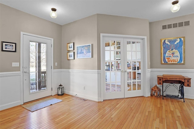 entrance foyer featuring visible vents, wood-type flooring, a wainscoted wall, and french doors