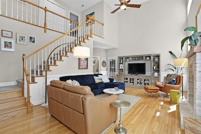 living area with hardwood / wood-style floors, a ceiling fan, baseboards, stairs, and a towering ceiling