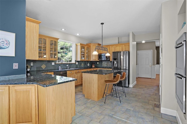 kitchen featuring tasteful backsplash, glass insert cabinets, a breakfast bar area, dark stone counters, and appliances with stainless steel finishes