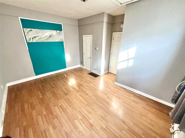 empty room with light wood finished floors, visible vents, and baseboards