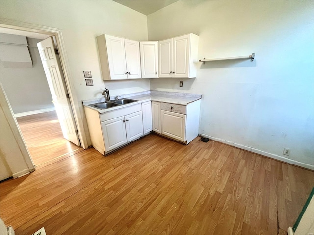 kitchen with baseboards, light wood-type flooring, light countertops, white cabinetry, and a sink