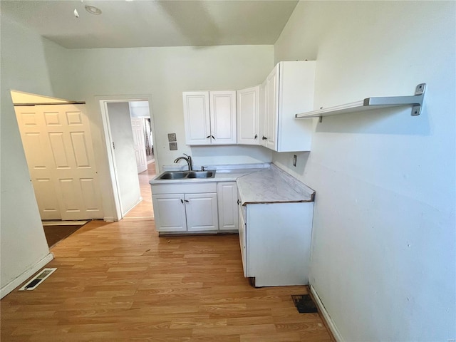 kitchen featuring visible vents, a sink, white cabinetry, light wood finished floors, and light countertops