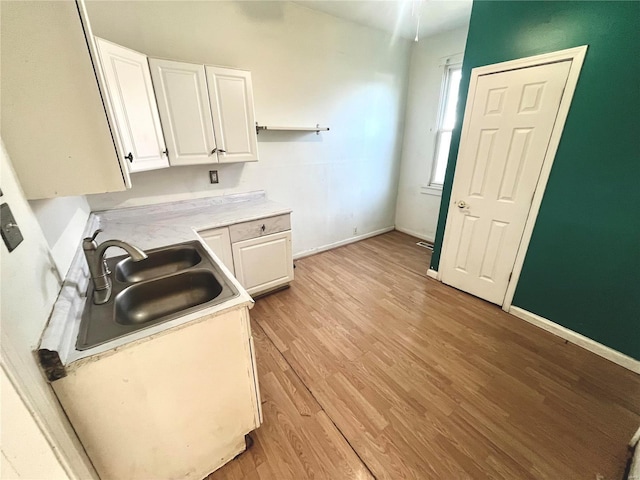 kitchen with light wood-type flooring, a sink, white cabinetry, light countertops, and baseboards