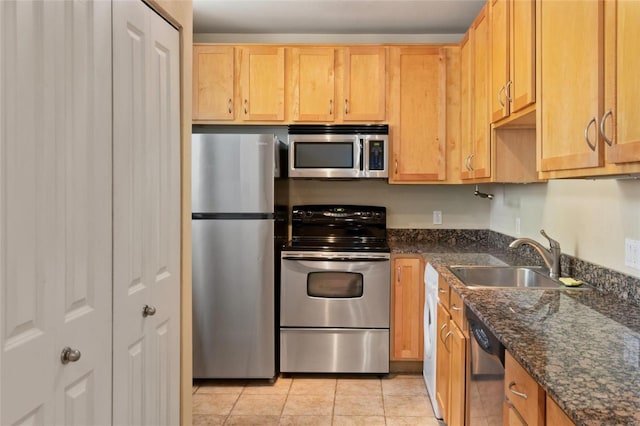 kitchen featuring light brown cabinetry, dark stone counters, appliances with stainless steel finishes, light tile patterned flooring, and a sink