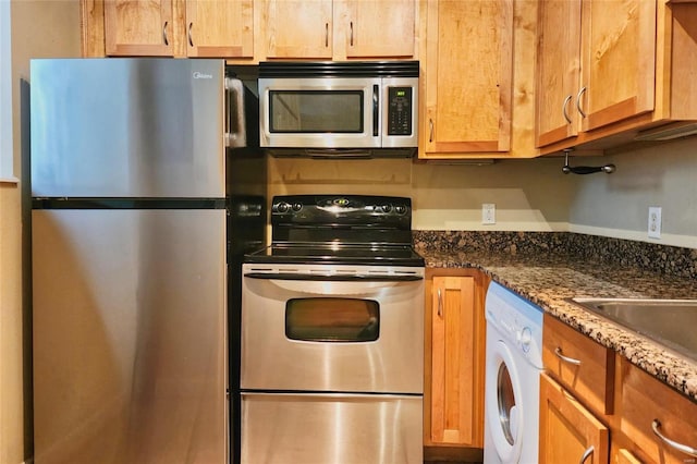 kitchen with dark stone counters, washer / clothes dryer, and appliances with stainless steel finishes