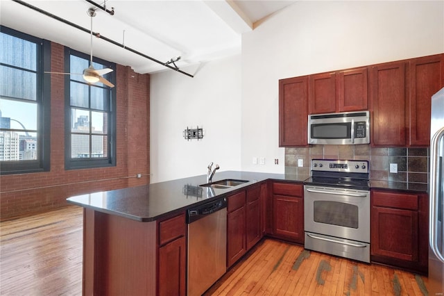 kitchen featuring light wood-type flooring, a sink, dark countertops, stainless steel appliances, and a peninsula