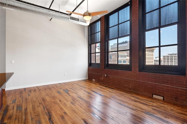 unfurnished room with hardwood / wood-style floors, visible vents, baseboards, brick wall, and a high ceiling