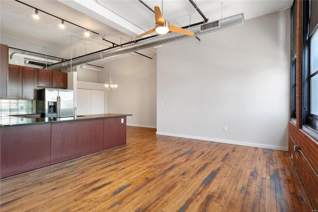 kitchen featuring hardwood / wood-style floors, baseboards, dark countertops, ceiling fan with notable chandelier, and stainless steel fridge