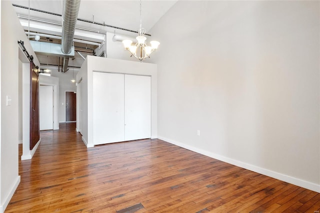 unfurnished dining area with baseboards, a high ceiling, wood-type flooring, a barn door, and a chandelier