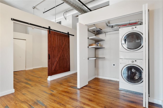 clothes washing area with baseboards, a barn door, stacked washer and dryer, laundry area, and hardwood / wood-style flooring