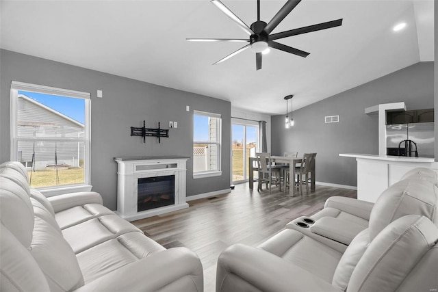 living area featuring visible vents, wood finished floors, a fireplace, lofted ceiling, and ceiling fan