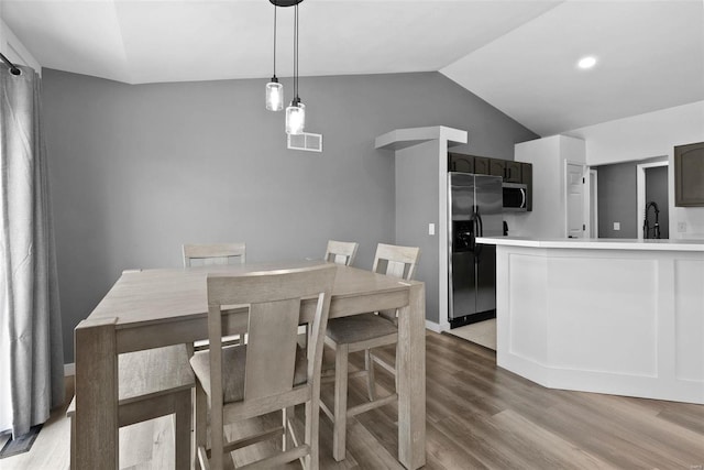 dining space featuring vaulted ceiling, light wood-style floors, visible vents, and baseboards