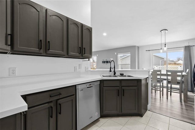 kitchen featuring a sink, stainless steel dishwasher, a peninsula, light countertops, and light tile patterned floors