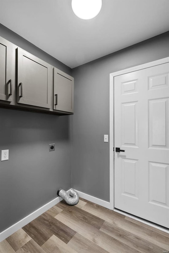 clothes washing area featuring cabinet space, electric dryer hookup, light wood-style flooring, and baseboards