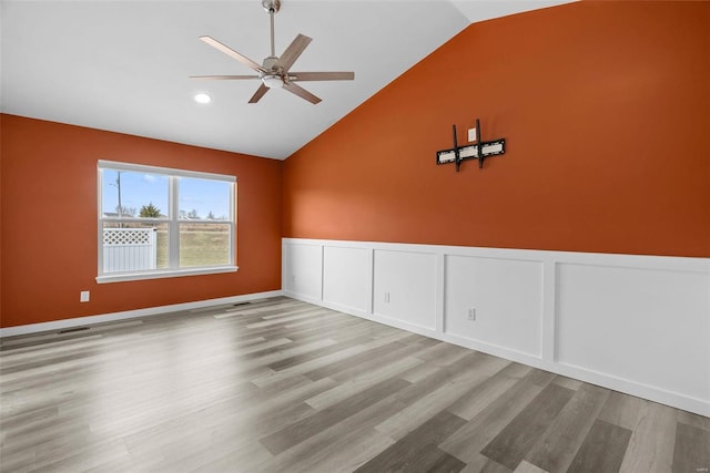 spare room with lofted ceiling, wood finished floors, wainscoting, and ceiling fan