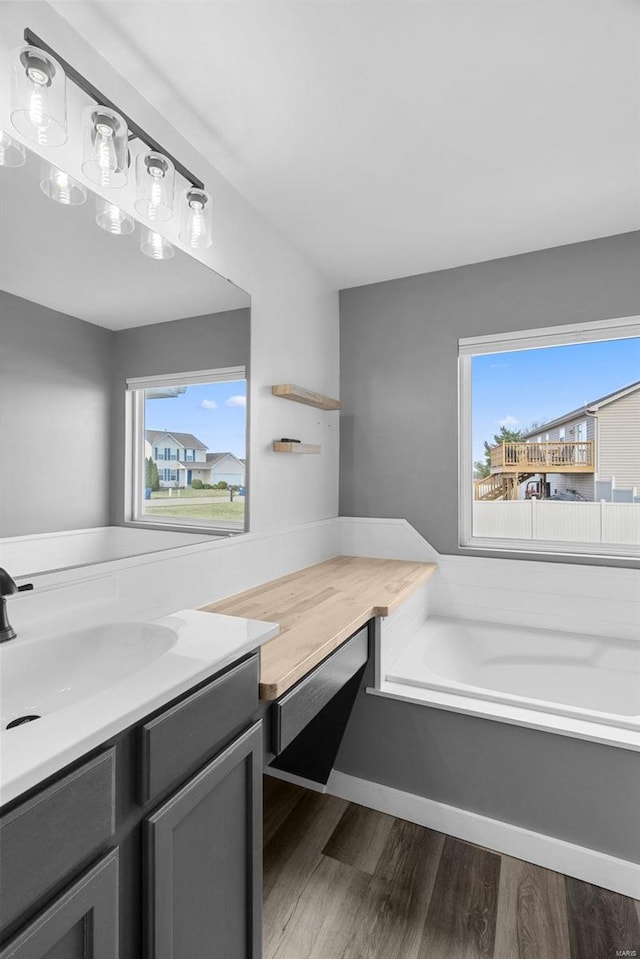 bathroom with vanity, a bath, wood finished floors, and baseboards