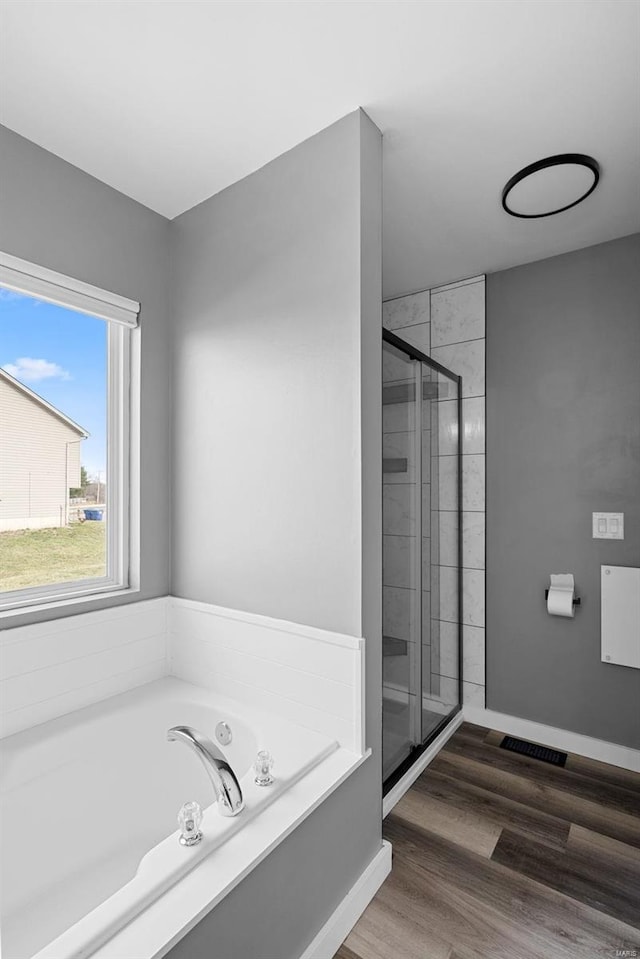 bathroom with a garden tub, wood finished floors, a stall shower, and baseboards