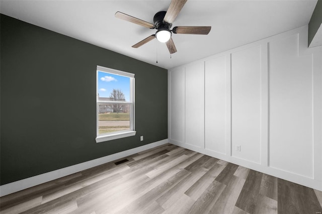 empty room featuring wood finished floors, baseboards, visible vents, ceiling fan, and a decorative wall